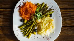 Top view of a vibrant vegetable salad featuring carrots, pickles, olives, and beans, served on a white plate.