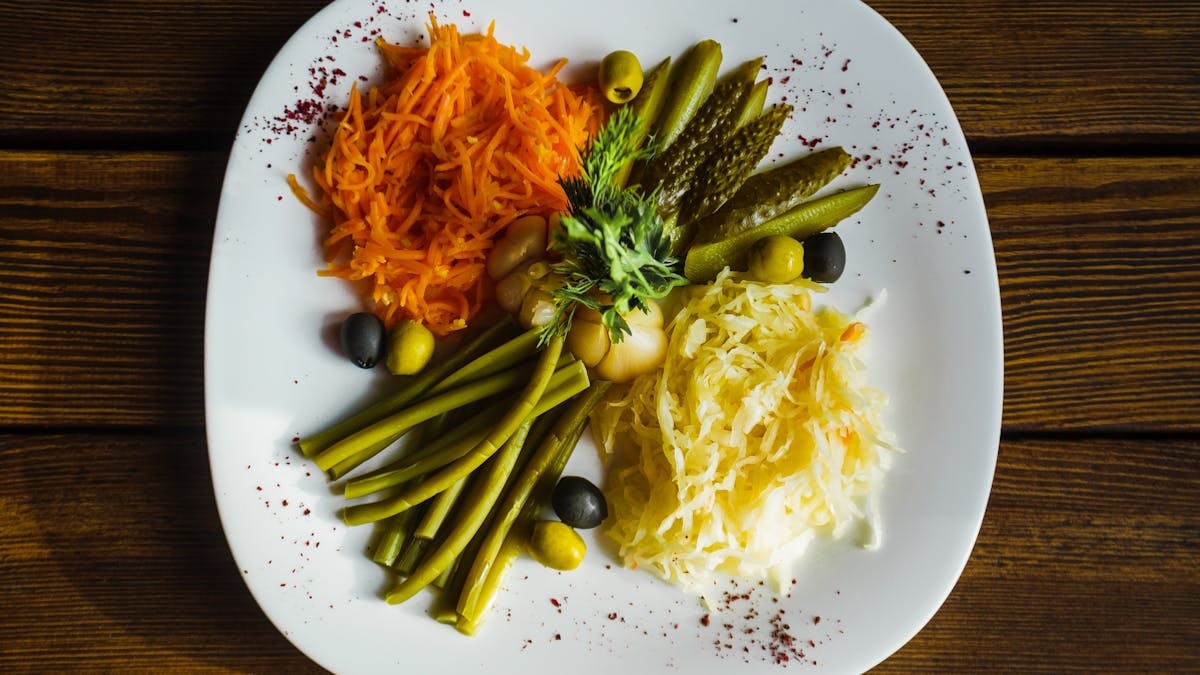 Top view of a vibrant vegetable salad featuring carrots, pickles, olives, and beans, served on a white plate.